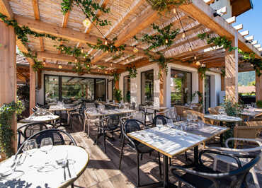 terrasse avec tables dressées sous pergolas en bois et végétaux