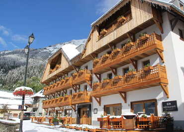 Bâtiment blanc avec balcons en bois, sol et sapins enneigés